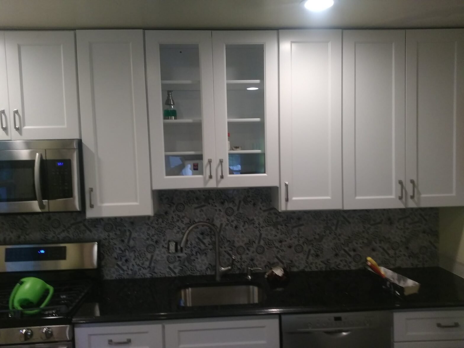 Finished kitchen with white glass-door cabinets, dark mosaic backsplash and black granite countertop