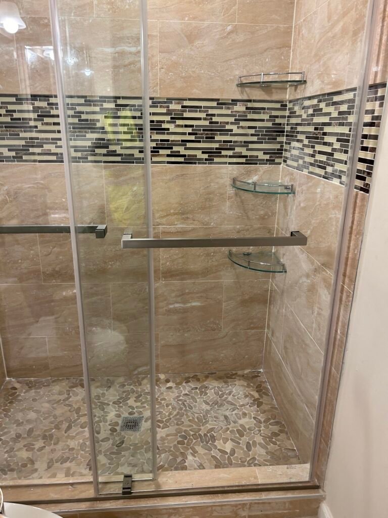 Sliding glass shower doors with decorative mosaic tile band in a remodeled Frederick bathroom
